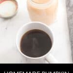 A white mug of black coffee sits beside a glass jar of Homemade Pumpkin Spice Creamer on a marble surface.