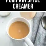 A white mug filled with coffee sits on a marble surface beside a gray cloth napkin and spoon, featuring the text "Homemade Pumpkin Spice Creamer" for a cozy, autumn-inspired touch.