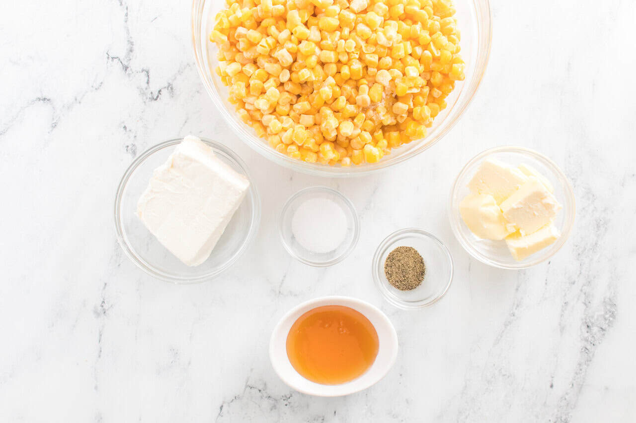 A bowl of veggies, cream cheese, butter, salt, pepper, and honey are arranged on a white marble surface.