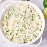 A white bowl filled sits on a white surface, a napkin, and a gold spoon.