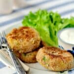 A fork on a plate with some pesto tuna fish patties and dipping sauce.