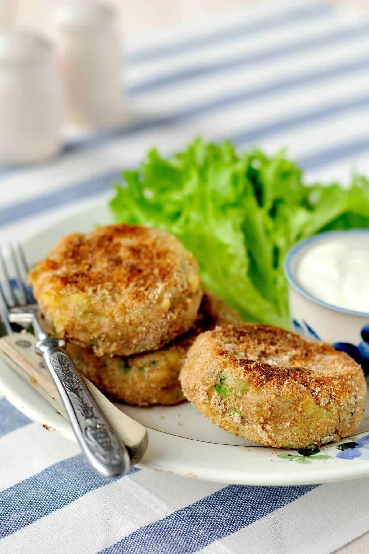 A fork on a plate with some pesto tuna fish patties and dipping sauce.