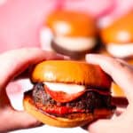 A hand holding a juicy hamburger.