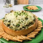 A green spinach cheesecake on a plate with crackers, perfect for those craving a flavorful Spinach and Artichoke Dip without Mayo.