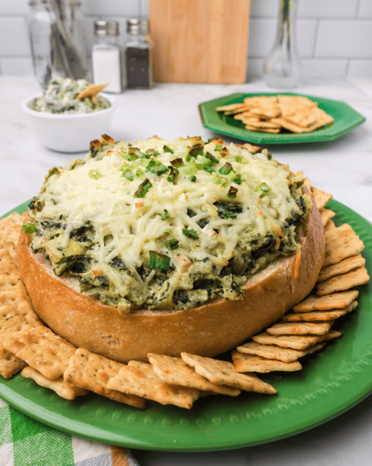A green spinach cheesecake on a plate with crackers, perfect for those craving a flavorful Spinach and Artichoke Dip without Mayo.