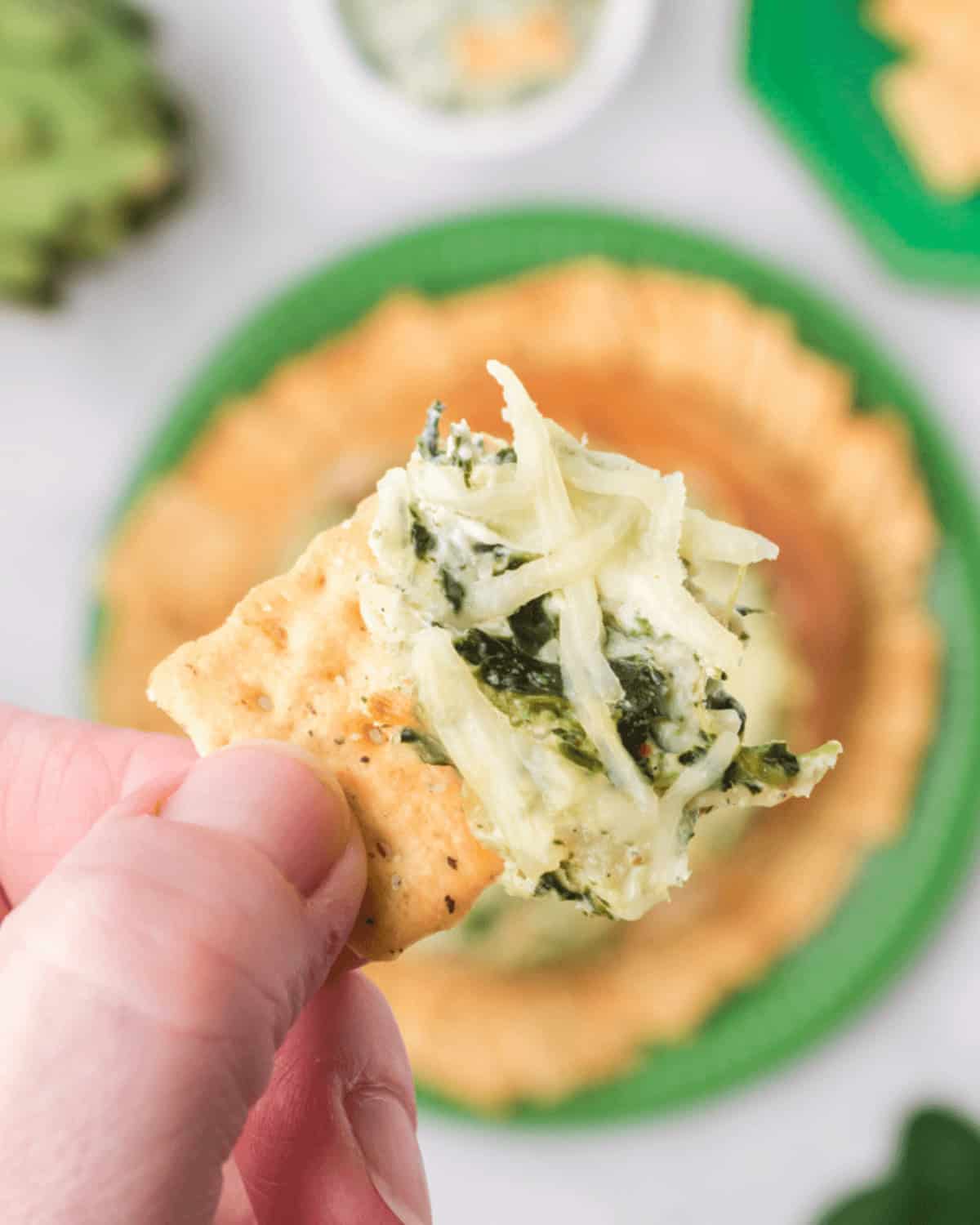 A person holding a cracker topped with spinach and cheese.