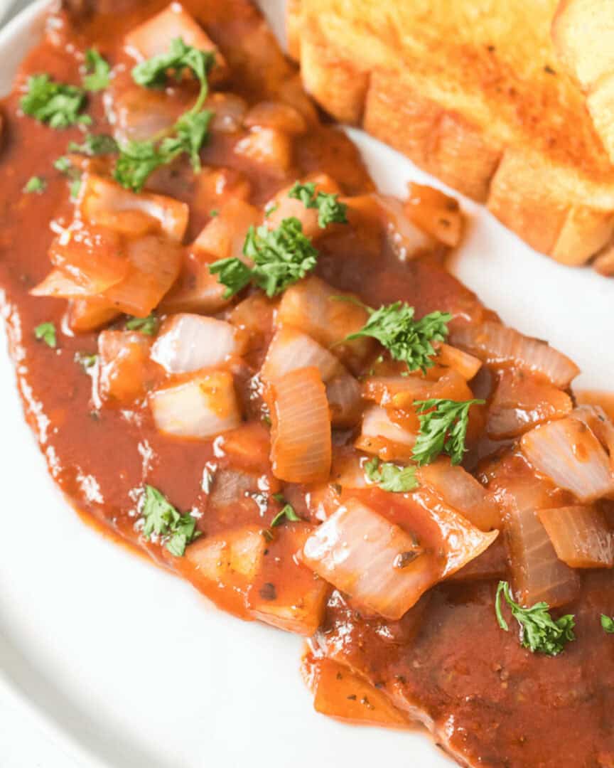 A delicious steak pizzaiola with a side of toast.