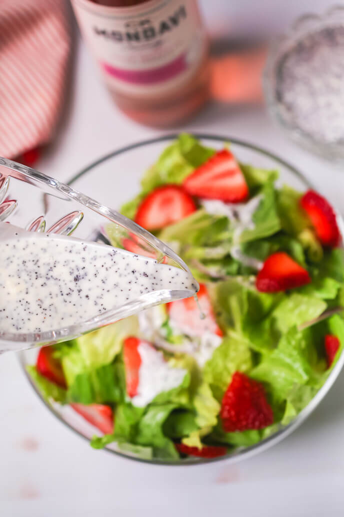 Dressing being poured on the Strawberry Poppyseed Salad.