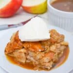 A slice of apple bread pudding with bourbon sauce is topped with vanilla ice cream on a white plate, accompanied by caramel sauce, fresh apple slices, and a knife in the background.
