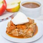 A slice of apple bread pudding with bourbon sauce, topped with vanilla ice cream and caramel sauce, sits center stage, while a bowl of sauce and sliced apples decorate the background.
