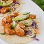 The meal with slaw, avocado slices, and sauce served on a white plate.