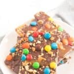 A plate of chocolate-covered toffee bars, similar to Caramel Pretzel Bark, topped with colorful candy-coated chocolates and chopped nuts.