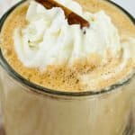 A glass mug filled with frothy Cinnamon Chocolate Latte topped with whipped cream and garnished with a cinnamon stick.