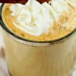 A glass of frothy Cinnamon Chocolate Latte topped with whipped cream and garnished with a cinnamon stick.