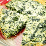 A slice of the quiche with the pie plate of spinach quiche.