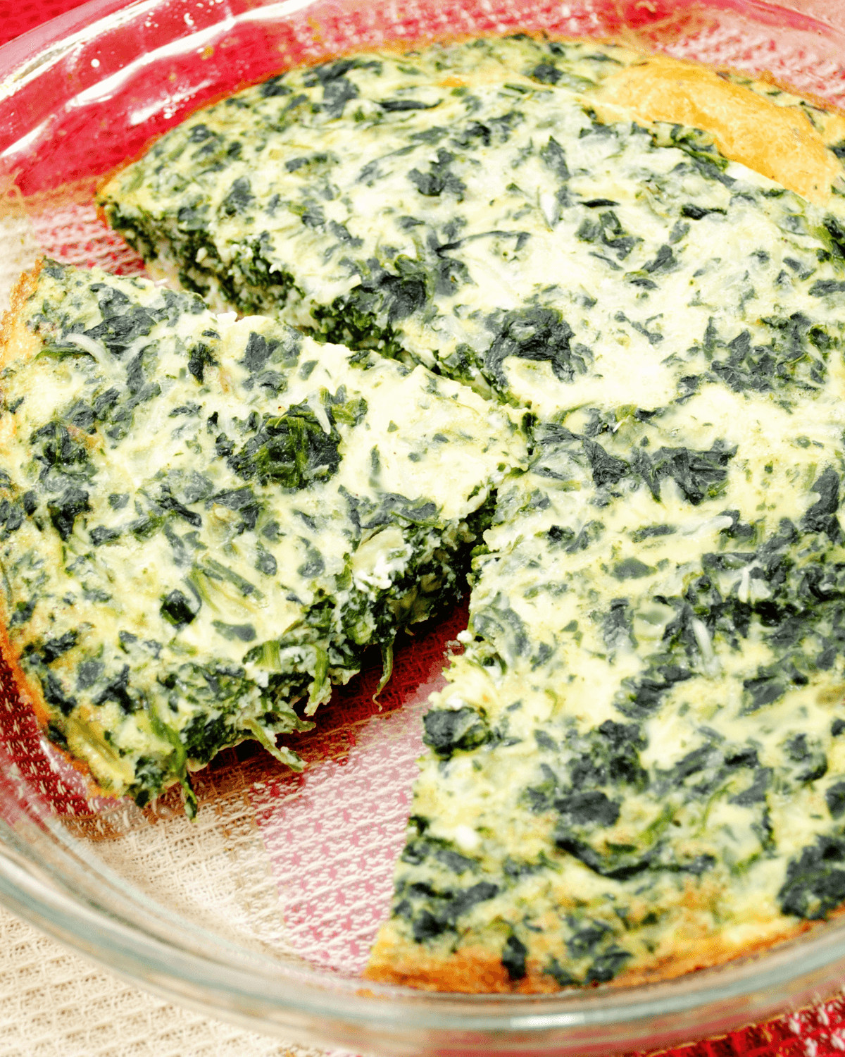 A slice of the quiche with the pie plate of spinach quiche.