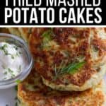 Golden-brown Fried Mashed Potato Cakes garnished with herbs, served on a plate with a side of sour cream in a small glass bowl.