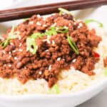 A Beef Bulgogi Bowl features a bowl of white rice topped with seasoned ground meat, garnished with sliced green onions and sesame seeds, with chopsticks in the background.