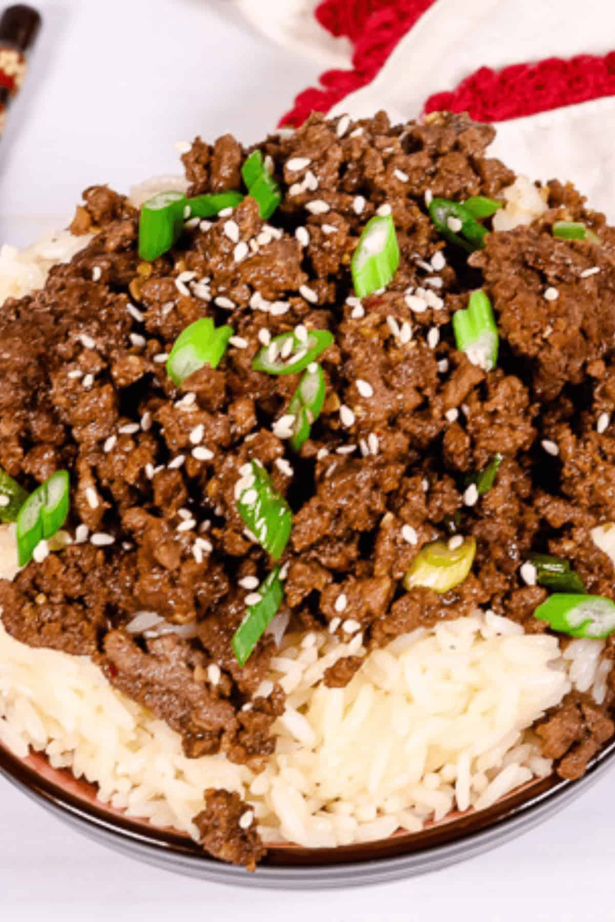 A Beef Bulgogi Bowl featuring a plate of white rice, topped with seasoned ground beef, and garnished with green onions and sesame seeds.