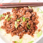 A Beef Bulgogi Bowl featuring a bed of rice crowned with seasoned ground beef, garnished with sliced green onions and sesame seeds, served alongside chopsticks.