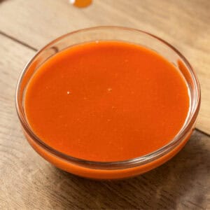A small glass bowl filled with zesty chicken wing sauce sits invitingly on a wooden surface.