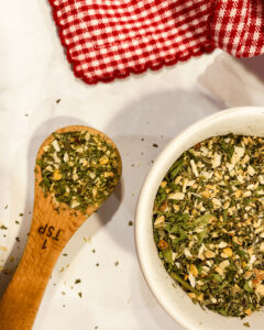 A heaping spoon of Italian Seasoning Substitute along side a bowl of the herbs.