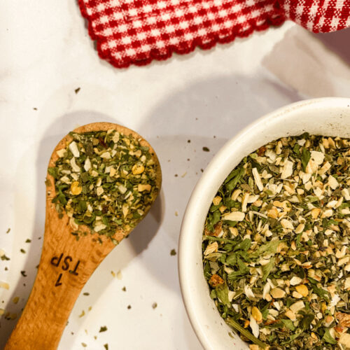 A heaping spoon of Italian Seasoning Substitute along side a bowl of the herbs.