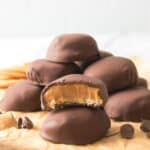 A stack of Peanut Butter Patties is shown on parchment paper, with one patty in front revealing a bite and its creamy peanut butter filling inside.