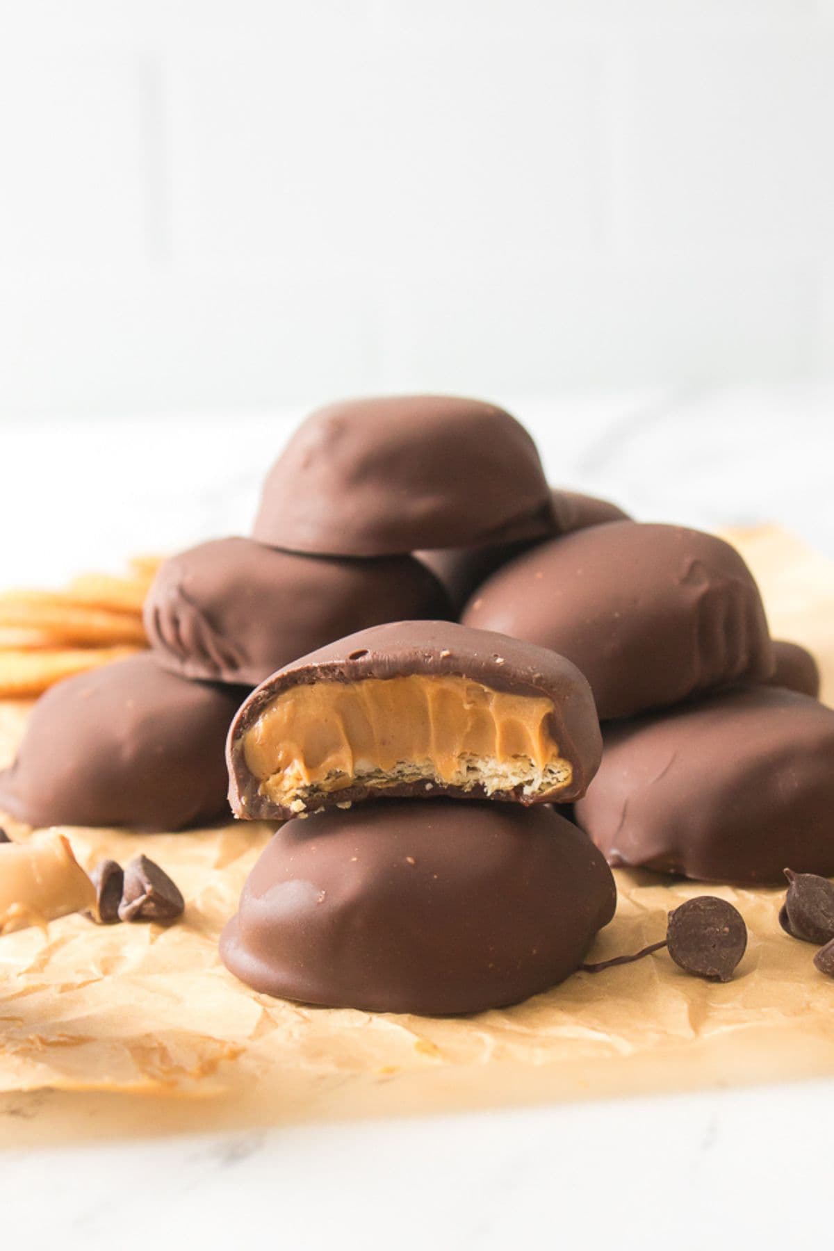 A stack of Peanut Butter Patties is shown on parchment paper, with one patty in front revealing a bite and its creamy peanut butter filling inside.