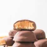 A stack of cookies coated in chocolate and filled with creamy peanut butter, with the top candy bitten to reveal the delicious inside.