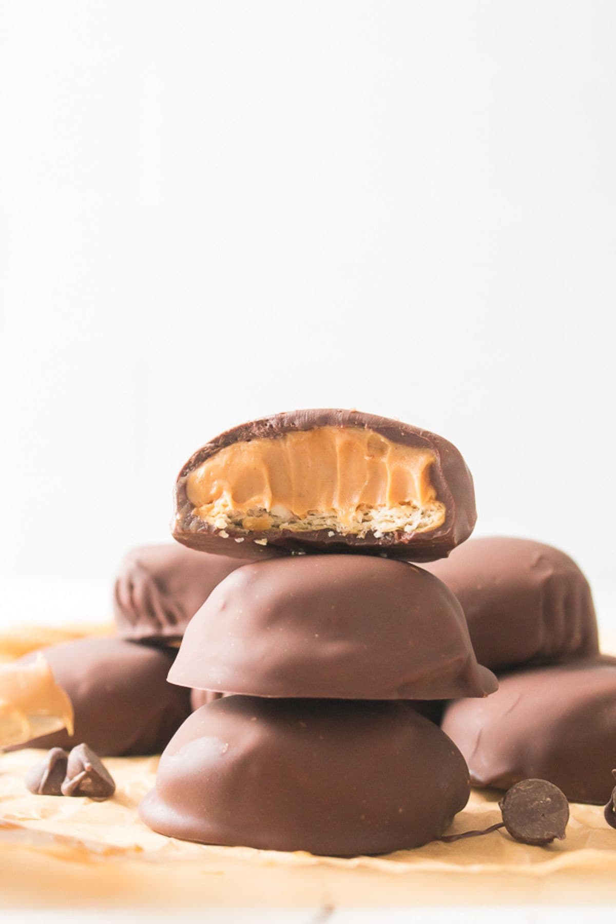 A stack of cookies coated in chocolate and filled with creamy peanut butter, with the top candy bitten to reveal the delicious inside.