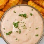 A bowl of Sheetz Boom Boom Sauce, rich and creamy, is garnished with parsley in the foreground. In the background, crinkle-cut fries are partially visible, ready to be dipped into this delicious blend.