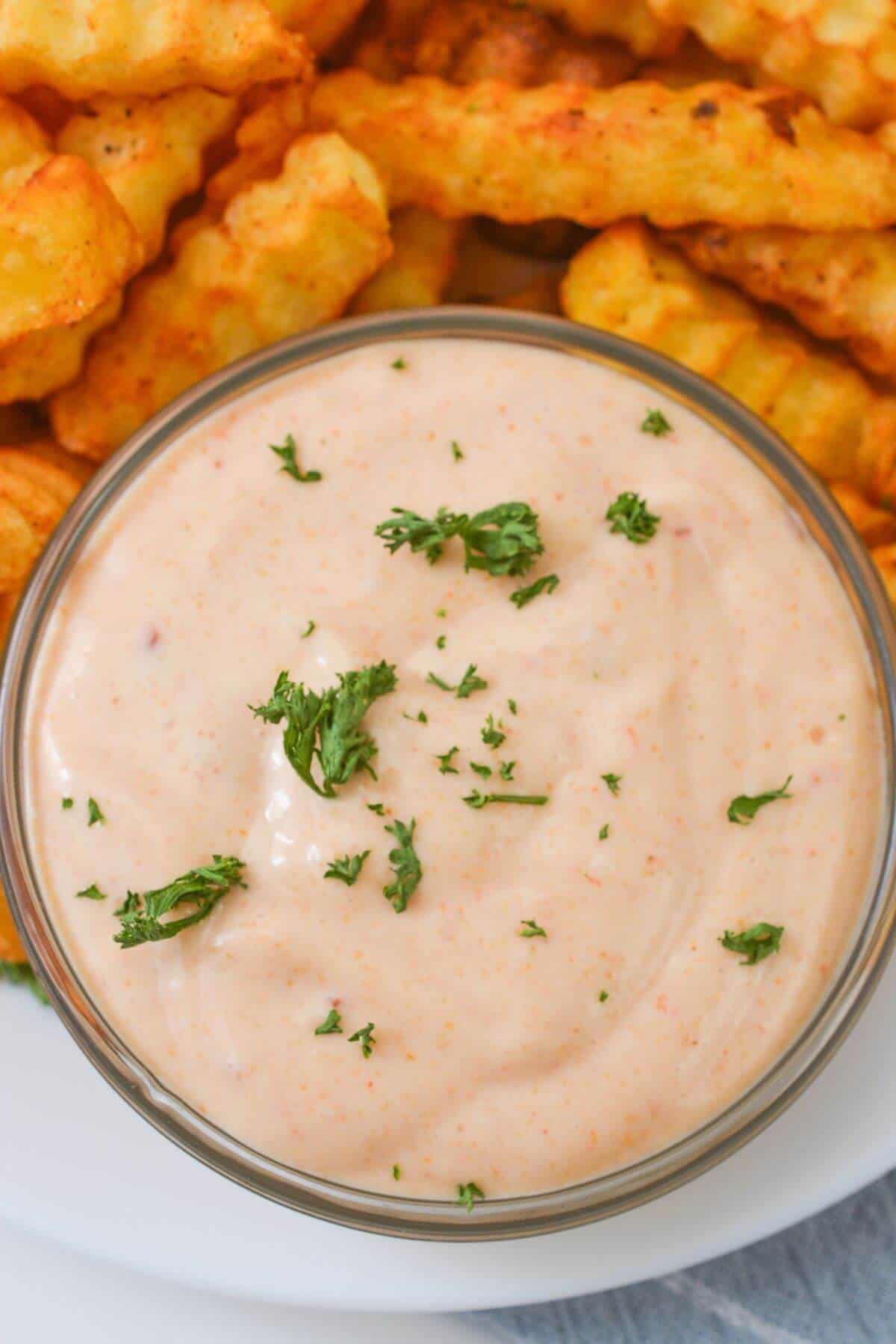 A bowl of Sheetz Boom Boom Sauce, rich and creamy, is garnished with parsley in the foreground. In the background, crinkle-cut fries are partially visible, ready to be dipped into this delicious blend.