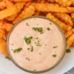 Crinkle-cut fries on a plate with a bowl of creamy Sheetz Boom Boom Sauce, garnished with chopped herbs.