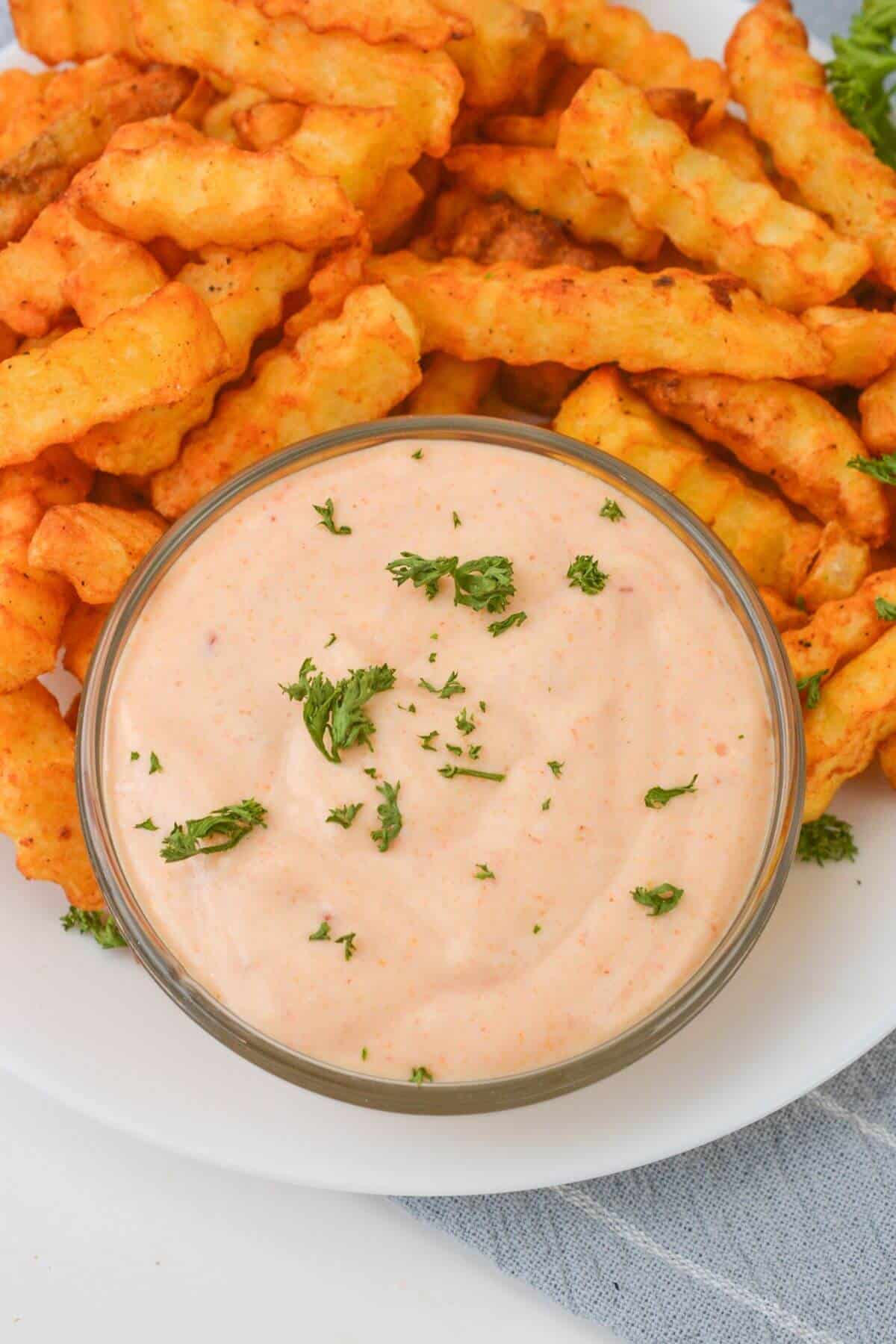 Crinkle-cut fries on a plate with a bowl of creamy Sheetz Boom Boom Sauce, garnished with chopped herbs.
