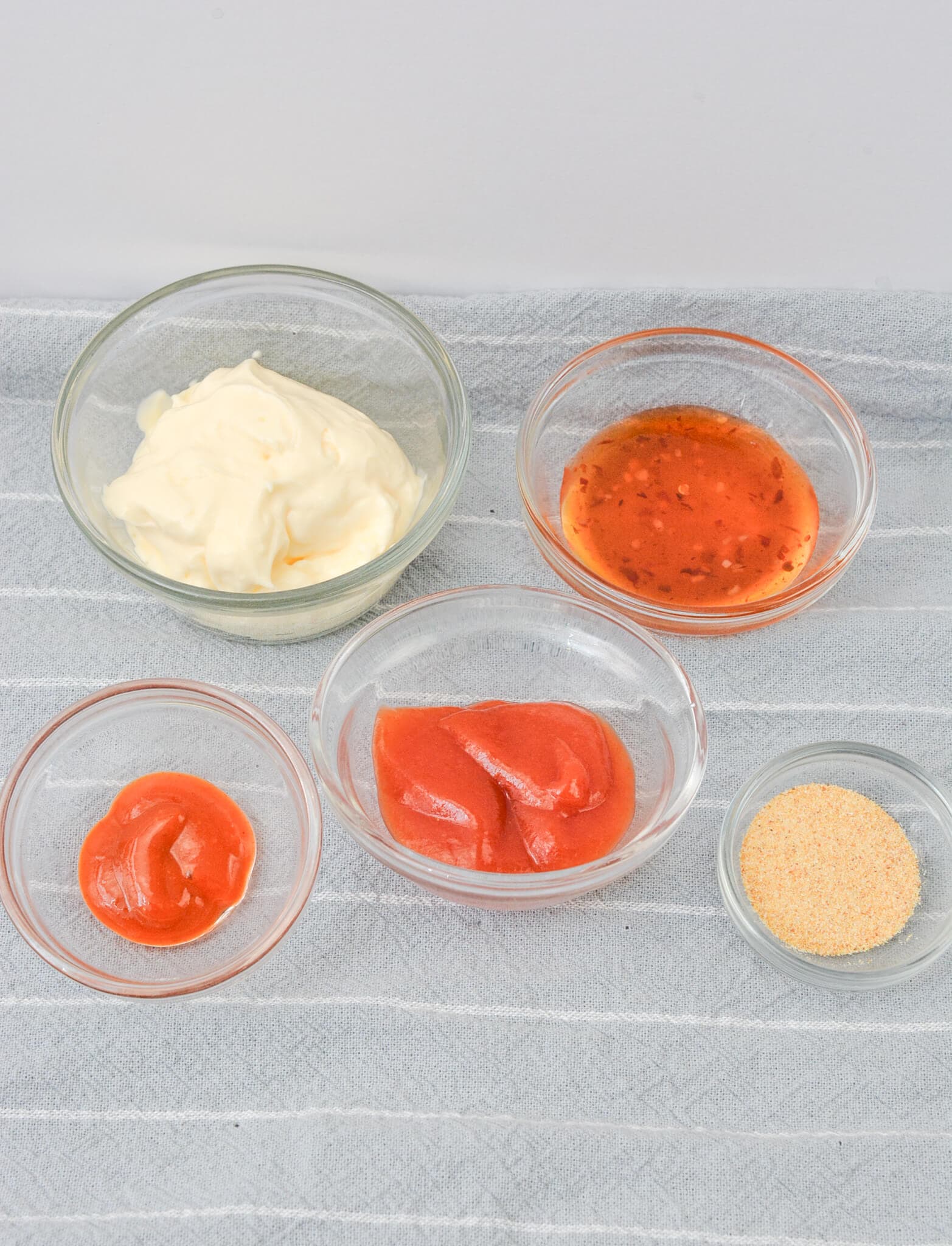 Five glass bowls containing mayonnaise, Sheetz Boom Boom Sauce, ketchup, another tangy sauce, and seasoning powder are placed on a striped cloth.
