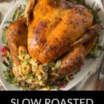 A whole Slow Roasted Turkey garnished with herbs and lemon slices is served on a white platter.