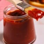 A glass jar filled with Chipotle BBQ Sauce with a basting brush resting on top, coated in the smoky, spicy sauce.