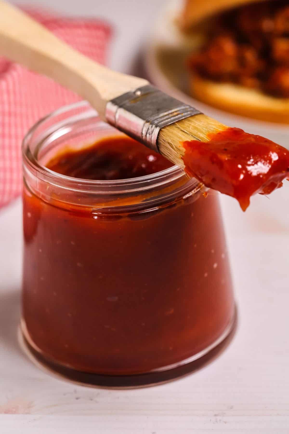 A glass jar filled with Chipotle BBQ Sauce with a basting brush resting on top, coated in the smoky, spicy sauce.