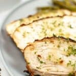 Close-up of sliced air fryer turkey breast garnished with chopped herbs, served on a gray plate with green beans in the background.