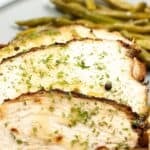 Sliced roasted meat garnished with herbs, served with green beans and roasted potatoes on a gray plate.