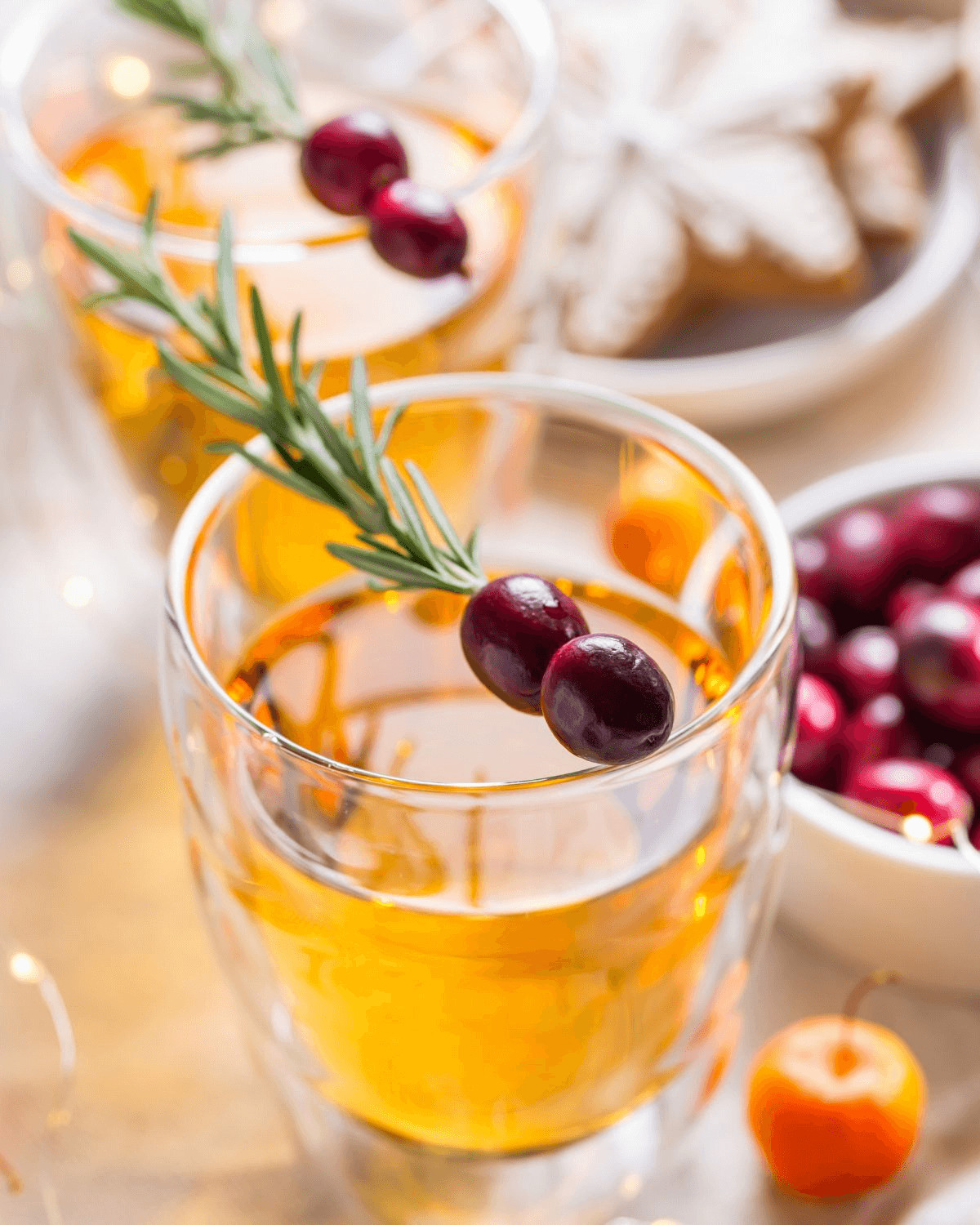 A glass of apple boilo with berries and a spring of rosemary.