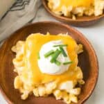 Macaroni and cheese portions sit on wooden plates, topped with melted cheese, sour cream, and chopped chives.