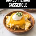 A wooden plate holds a savory baked pierogi casserole, adorned with melted cheese, a dollop of sour cream, and a sprinkle of chopped chives. Set against the sleek elegance of a marble countertop background.