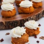 Mini Cake Mix Pumpkin Spice Cookies topped with white frosting are arranged on a rustic wooden platter, with two cookies and scattered pecan pieces in the foreground.