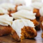 The treat with white frosting, one of which has a bite taken out, displayed on a wooden surface.