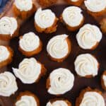Mini cupcakes with white swirled frosting are arranged on a wooden serving platter with a blue cloth partially visible underneath, alongside delightful Cake Mix Pumpkin Spice Cookies for a cozy treat display.