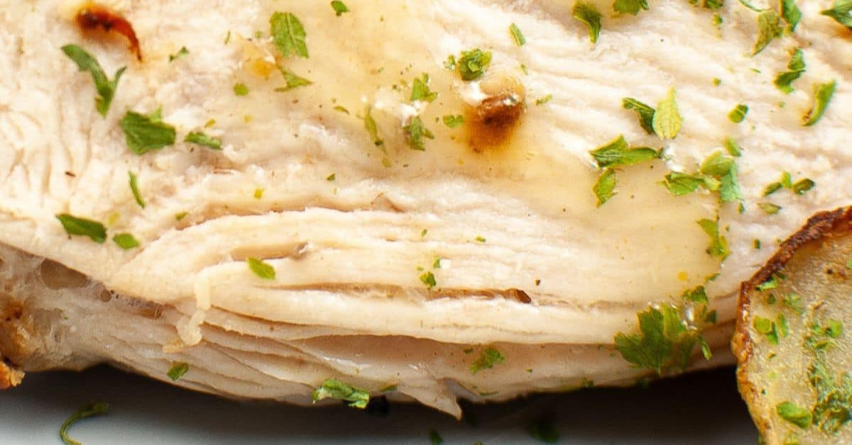 Close-up of a cooked breast garnished with chopped herbs, with a slice of roasted potato on the side—perfect inspiration for preparing Air Fryer Turkey Breast with similar flavors and presentation.