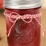 A glass jar filled with the drink sealed with a metal lid and decorated with a red and white striped string tied in a bow around the top.