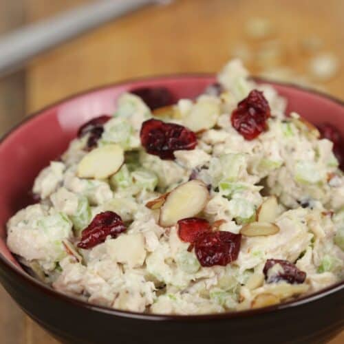 A bowl of Cranberry Turkey Salad mixed with celery, sliced almonds, and dried cranberries sits on a wooden surface.
